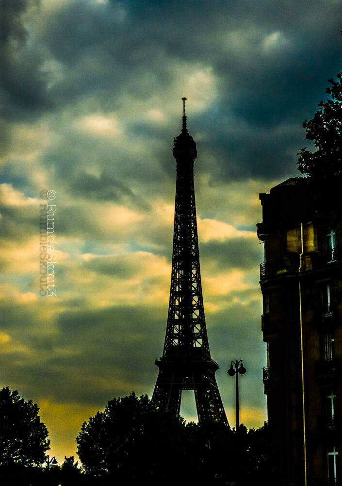 In the long sunset afterglow of Paris a silhouette of the Eiffel Tower outlines the sky, reminiscent of a 30s Paris noir film in the 7th arrondissement de Paris.