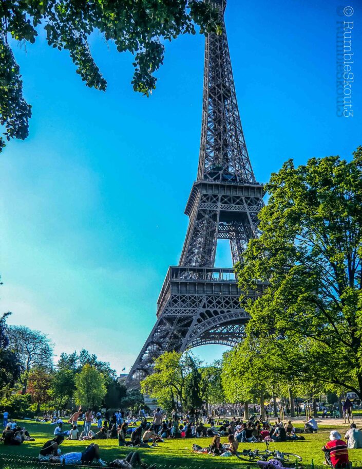 A dude enjoying a lazy Sunday late afternoon as people near and below the Eiffel Tower gather in 7th arrondissement de Paris. A Chillin Red Shirt with a White Hat on the Champs de Mars
