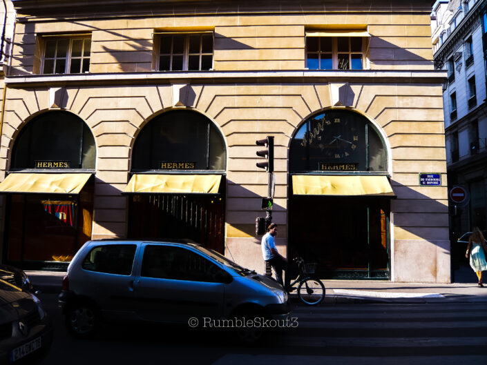 A morning bicyclist in front of Hermès Paris waits at 24 Rue du Faubourg Saint-Honoré in the 8th arrondissement of Paris. OG (paris street photography)
