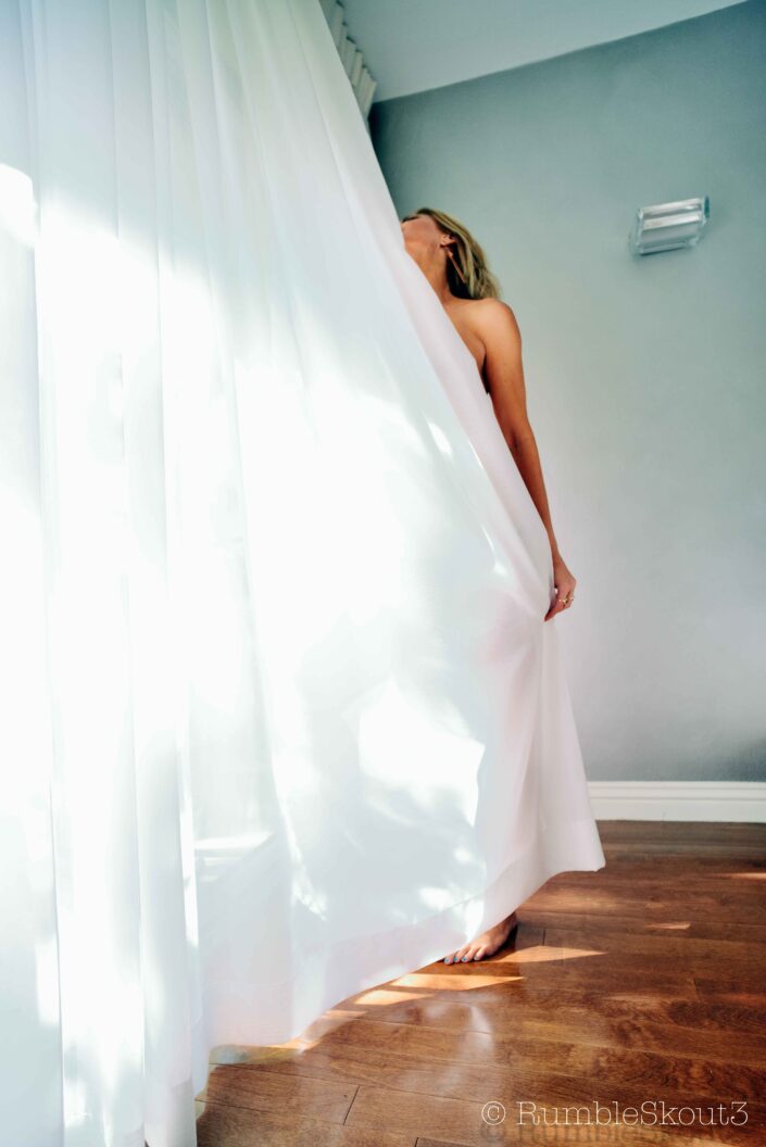 A nude blonde model frolics and dances her Sol out to White Wedding (Window Play on Flores St) on her playlist for a fine art natural light fashion session in California sunlight, West Hollywood.