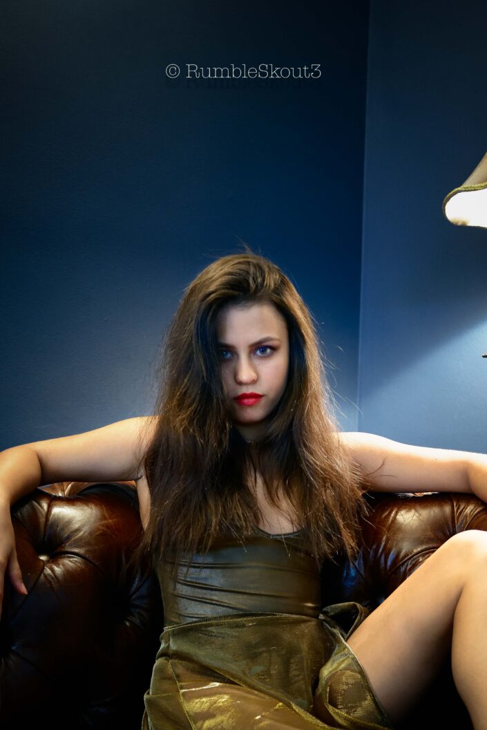 An American Élégance Bella in an Art Déco Azul Salon, with amber eyes, in a bodysuit sheer dress, on a leather chesterfield sofa sitting for an American woman portrait in West Hollywood, contemplating Mars.