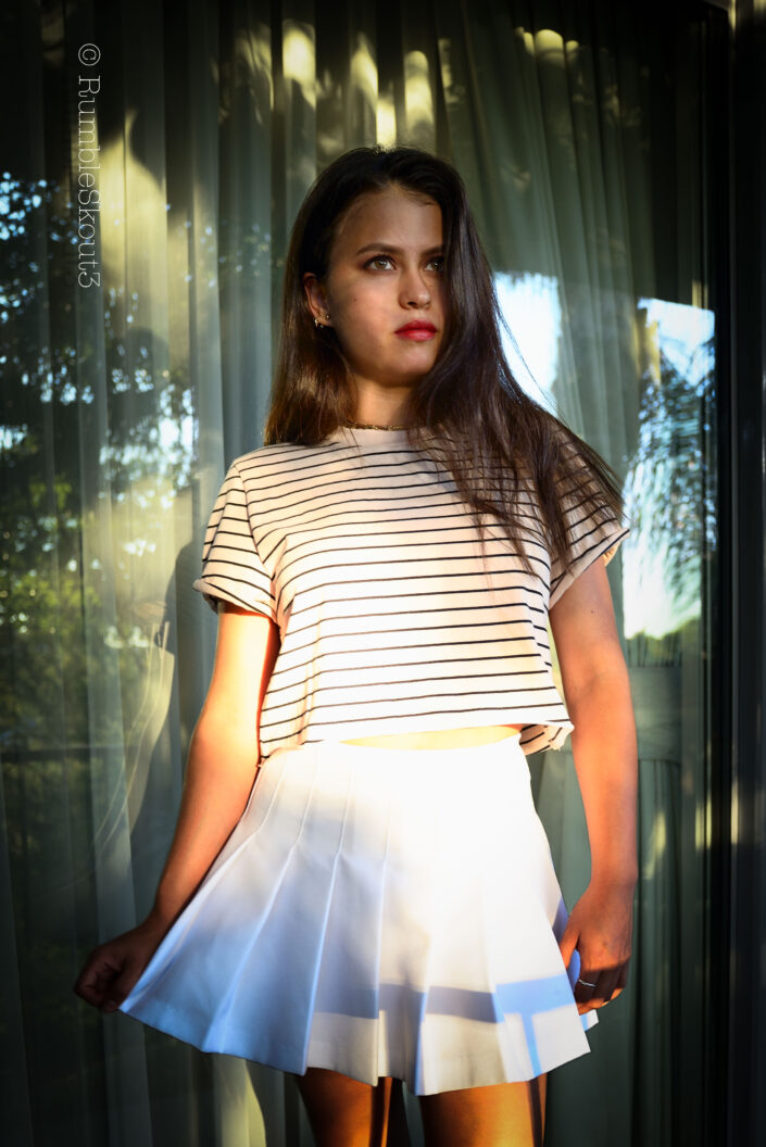 An Indigenous Mexican Nikon fine art Natural Light Fashion Photography session of an aspiring Hilfiger Fashion Model in women's striped top and pleated tennis skirt with amber-eyes-American beauty fashion model.
