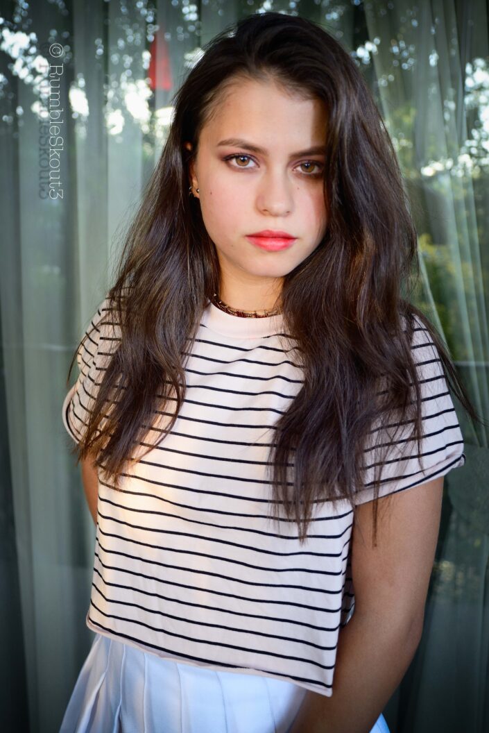 An Indigenous Mexican Nikon fine art Natural Light Fashion Photography session of a Nueva Salvadoreña Estrella Hilfiger Fashion Model in women's striped top and pleated tennis skirt with amber-eyes-American beauty fashion model.