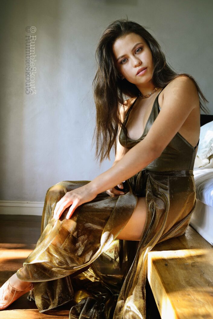 Golden Selena, with amber eyes, in a natural light fashion photography session for an American woman portrait in a bodysuit sheer dress, sitting on an Environment Santos Platform Bed in an Alta California Golden Room, West Hollywood. Selena Oro ( XII)