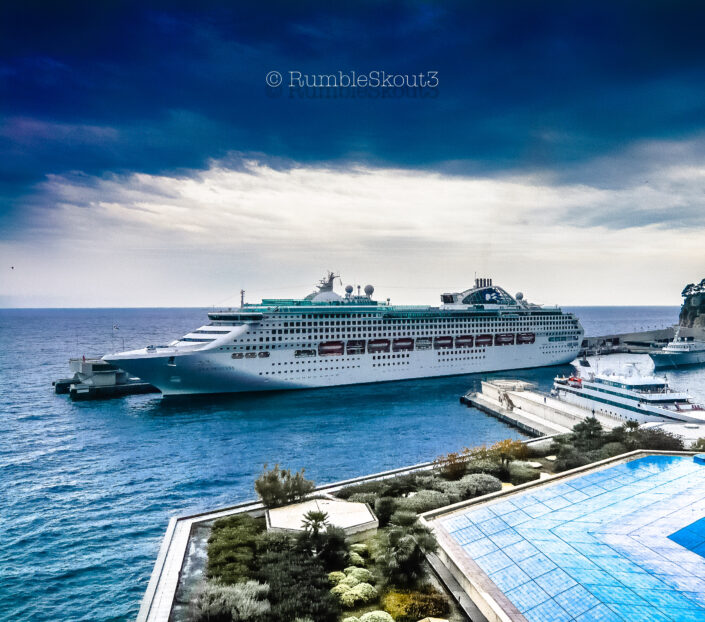 A docked cruise ship with a blue Mediterranean sea in the distance, in a marina at Port Hercule in Monaco French Riviera Côte d'Azur.
