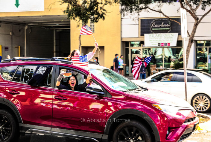 (Red SUV) (Year 2020 Los Angeles) (2020 Joe Biden Election Celebration) (Santa Monica Blvd) (West Hollywood) (waving U.S. flags) (cheering crowd)